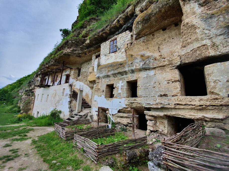 Historic cave monastery carved into limestone cliff with traditional wooden gates