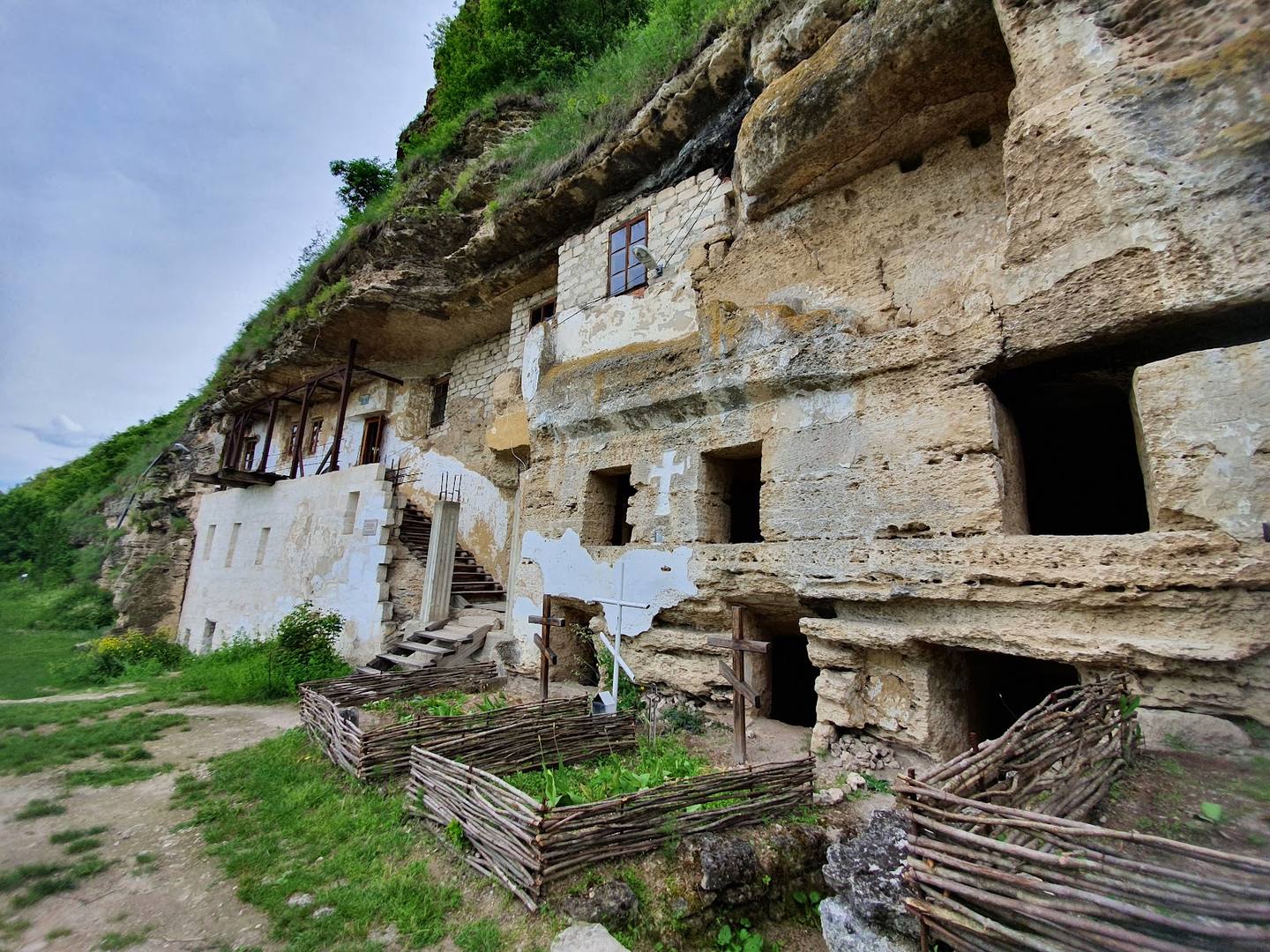 Historic cave monastery carved into limestone cliff with traditional wooden gates
