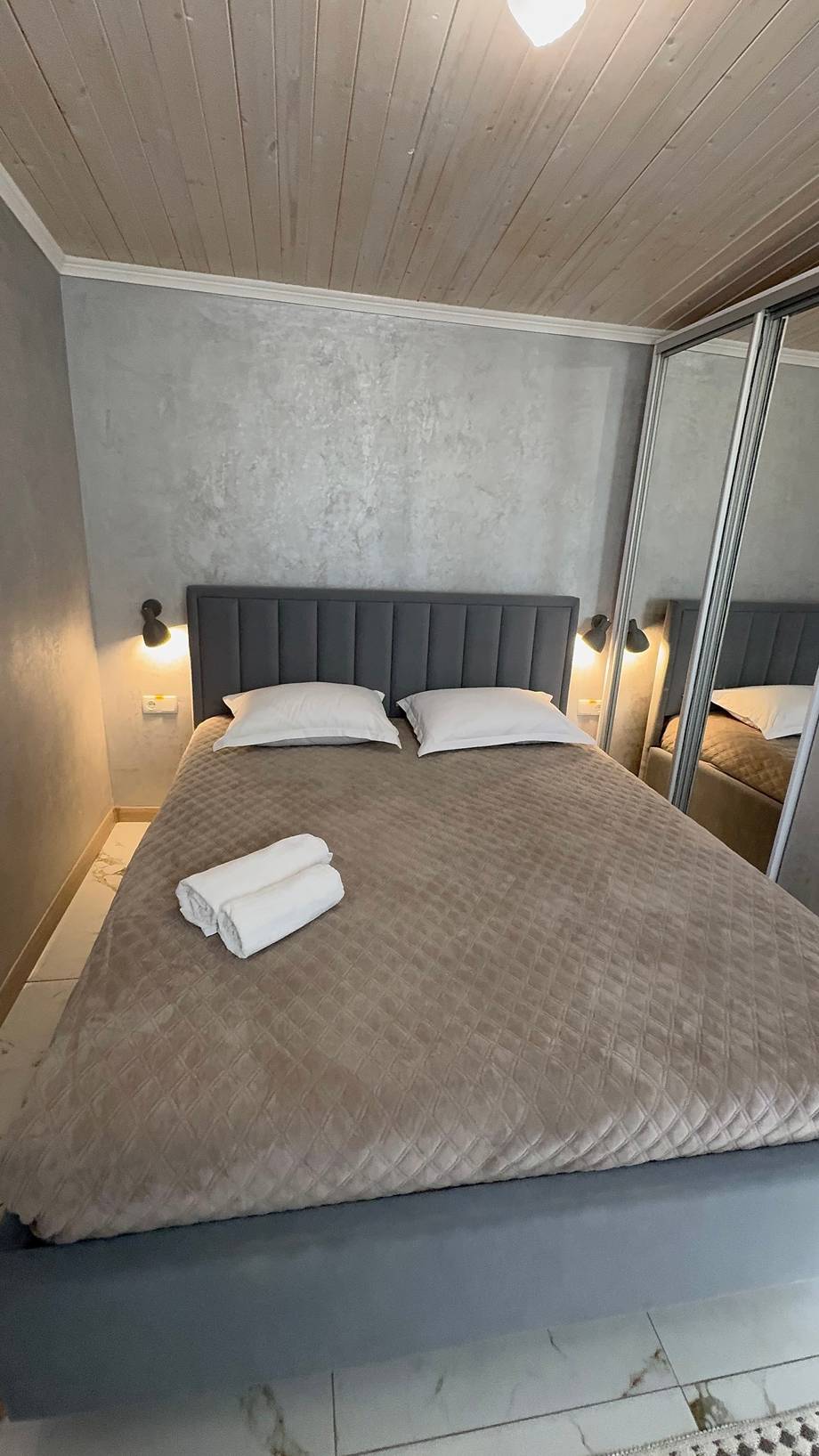 Modern bedroom with upholstered headboard, wood ceiling, and mirror closet doors