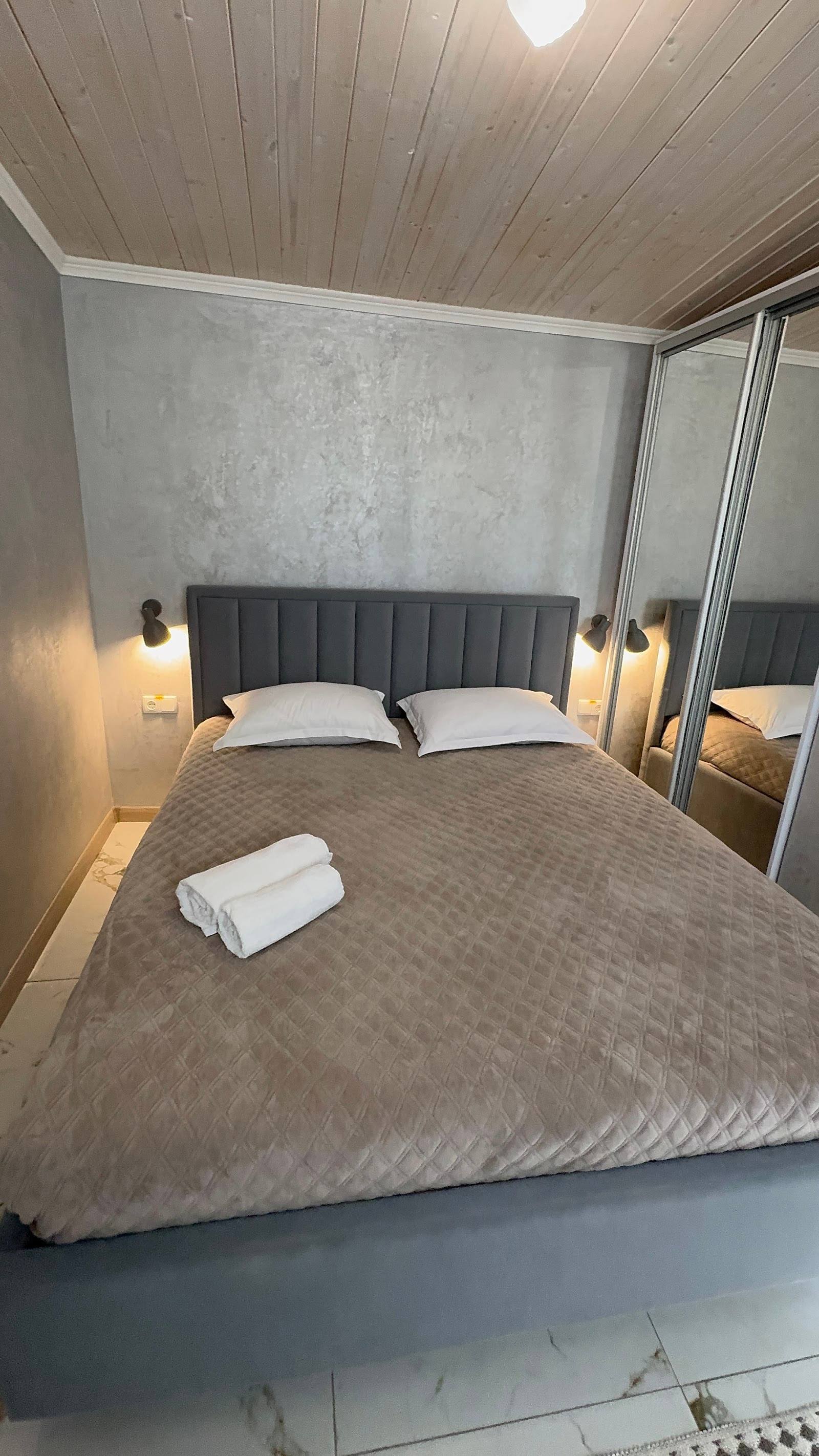 Modern bedroom with upholstered headboard, wood ceiling, and mirror closet doors