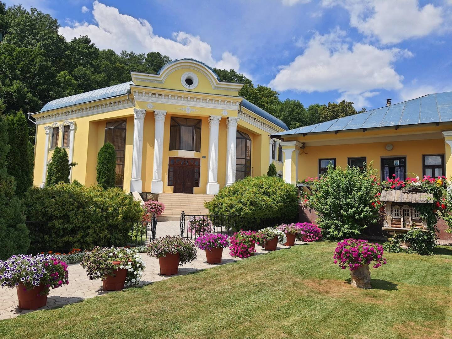 Yellow neoclassical building exterior with manicured gardens and flowering landscaping
