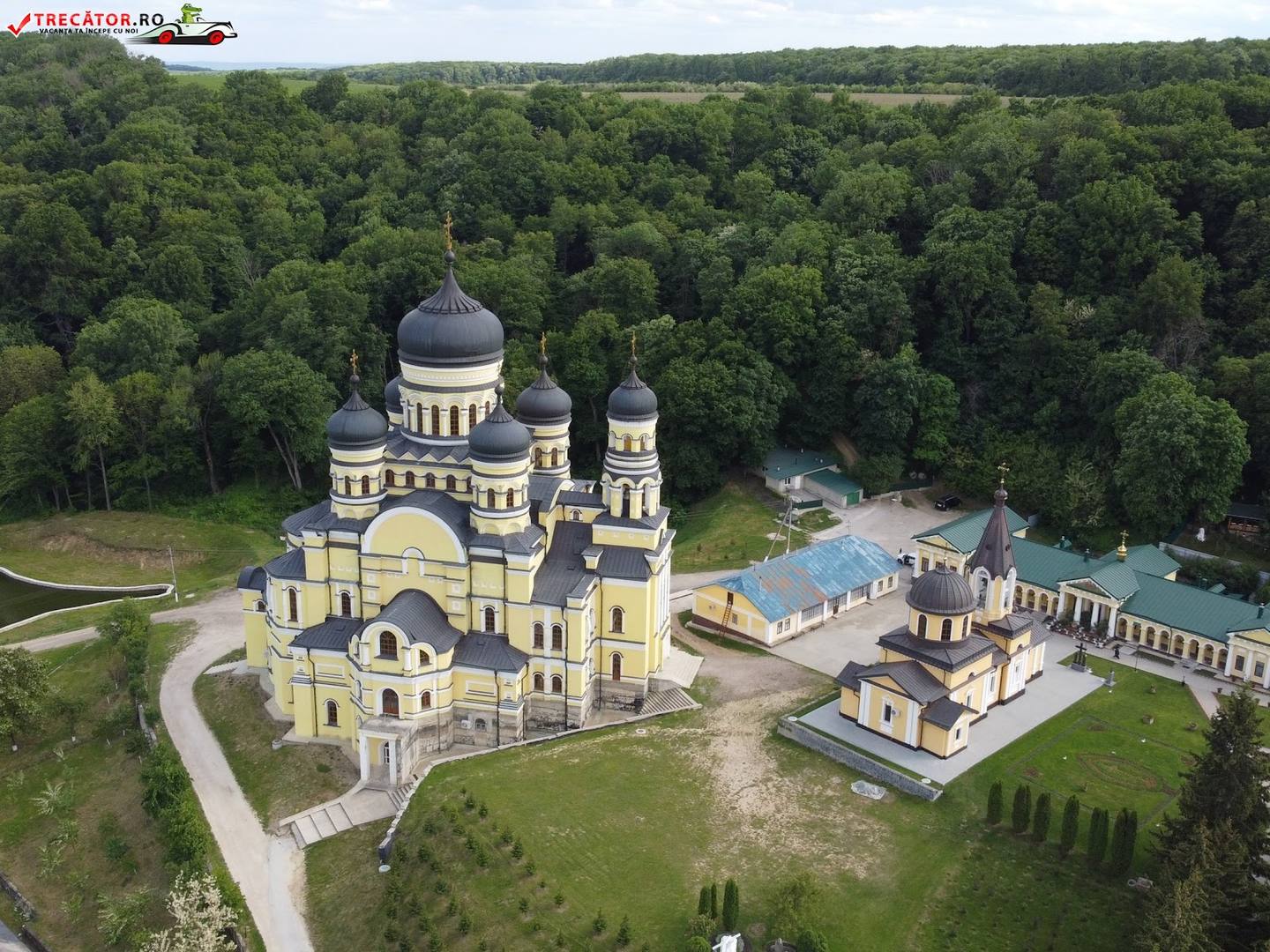 Aerial view of Orthodox monastery with golden domes and surrounding grounds nestled in forested landscape