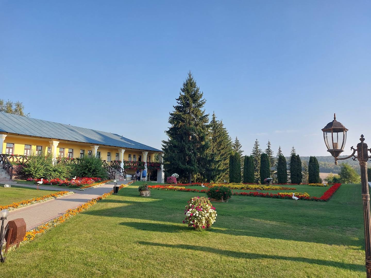 Manicured grounds with lodge building, landscaped gardens, and tall evergreen trees in daylight