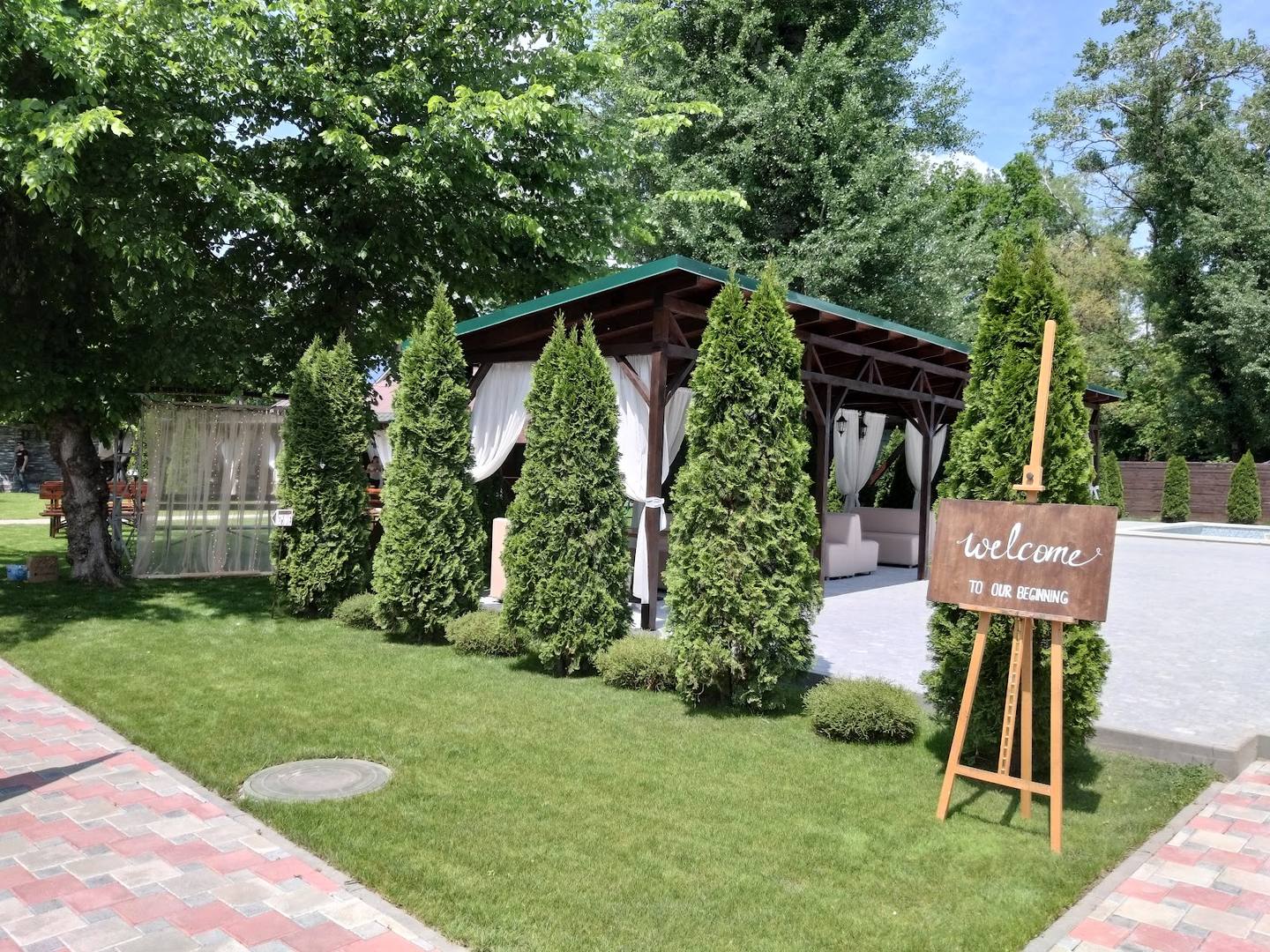 Modern garden pavilion with ivy-covered arbor and welcome sign on manicured grounds