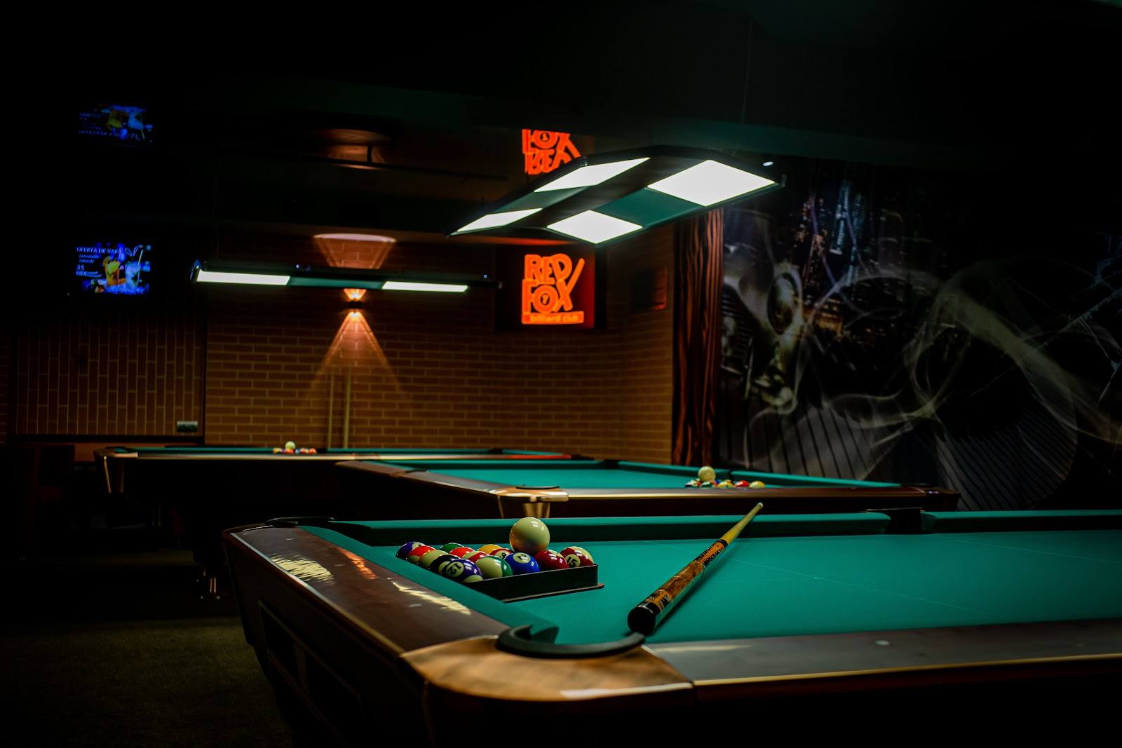 Pool table setup in dimly lit billiards hall with neon signage and street art