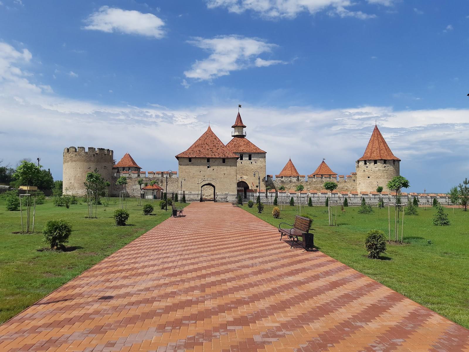 Fortified monastery with distinctive turrets and brick pathway approach under blue sky