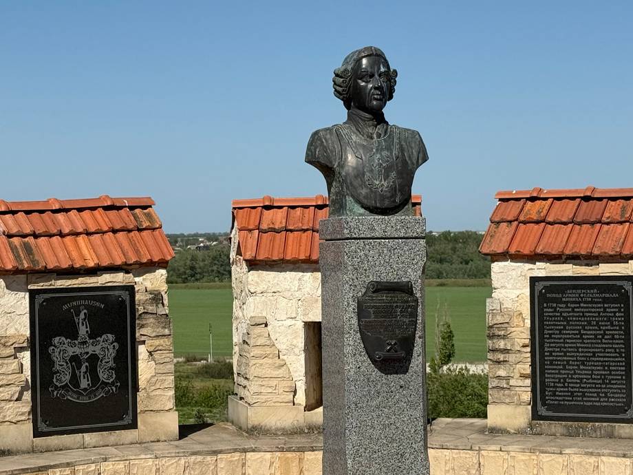 Bronze bust monument with memorial plaques overlooking open countryside
