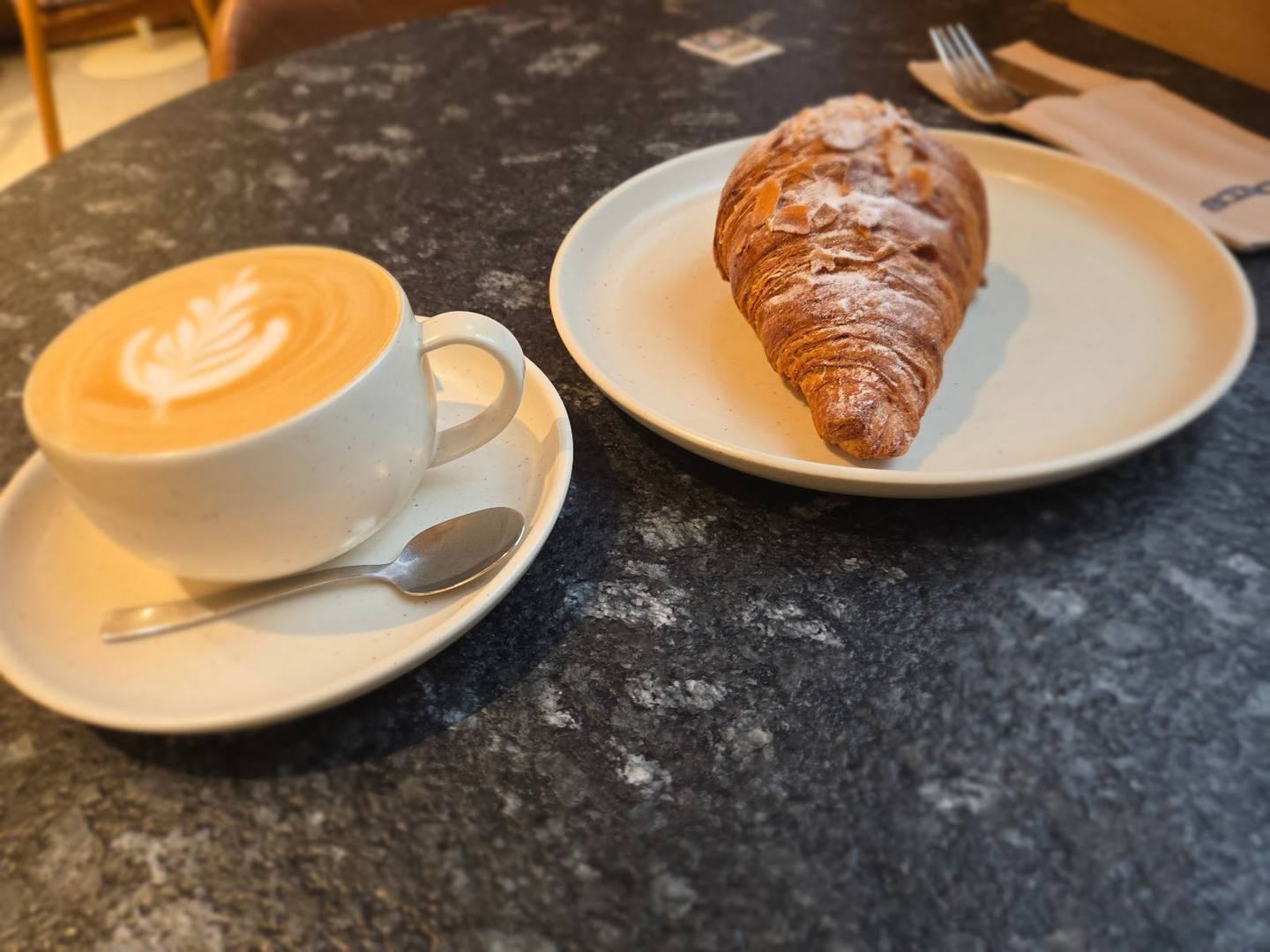 Cappuccino with latte art and fresh croissant on dark stone table