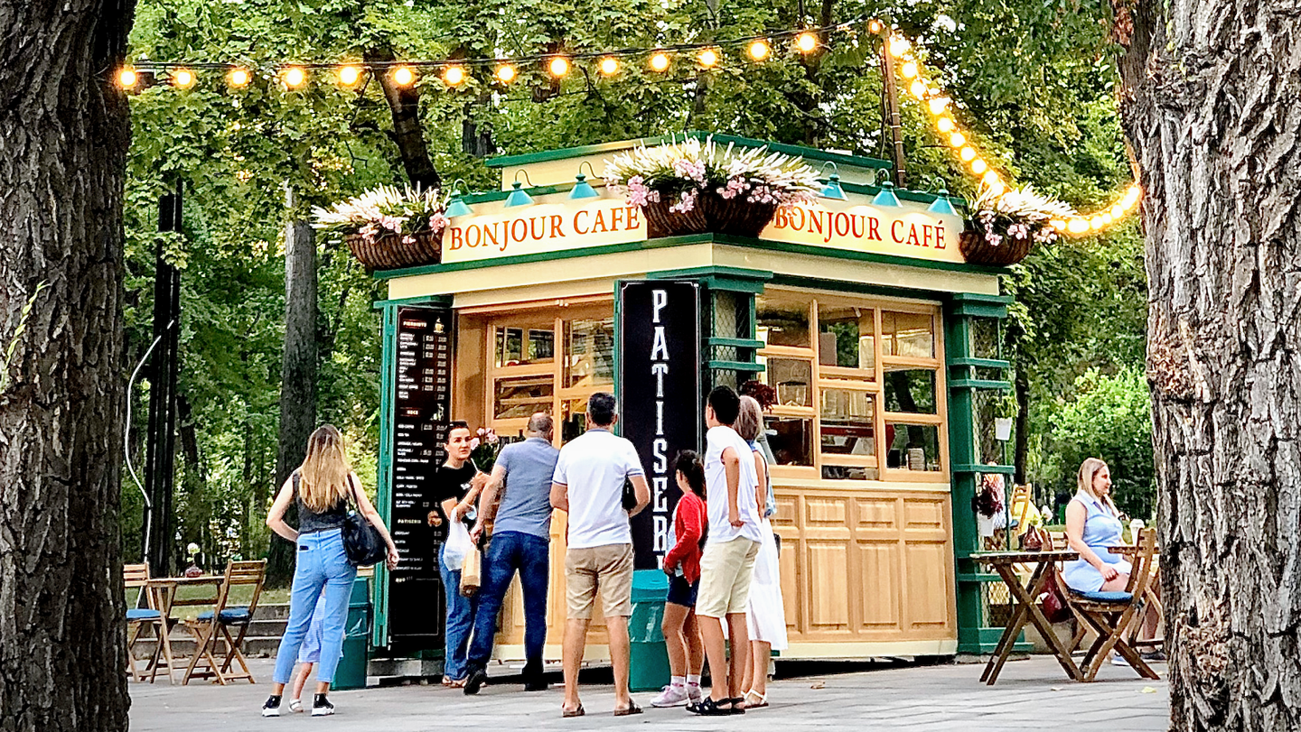 Compact outdoor kiosk café with wooden structure and green signage nestled between trees