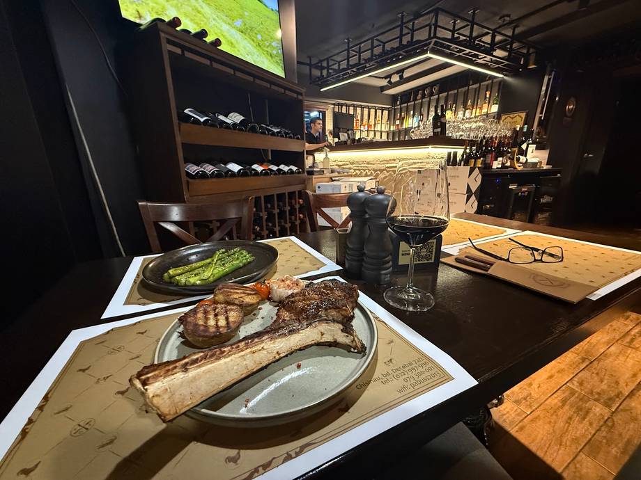 Grilled meat and vegetables plated at upscale restaurant with bar setup visible in background