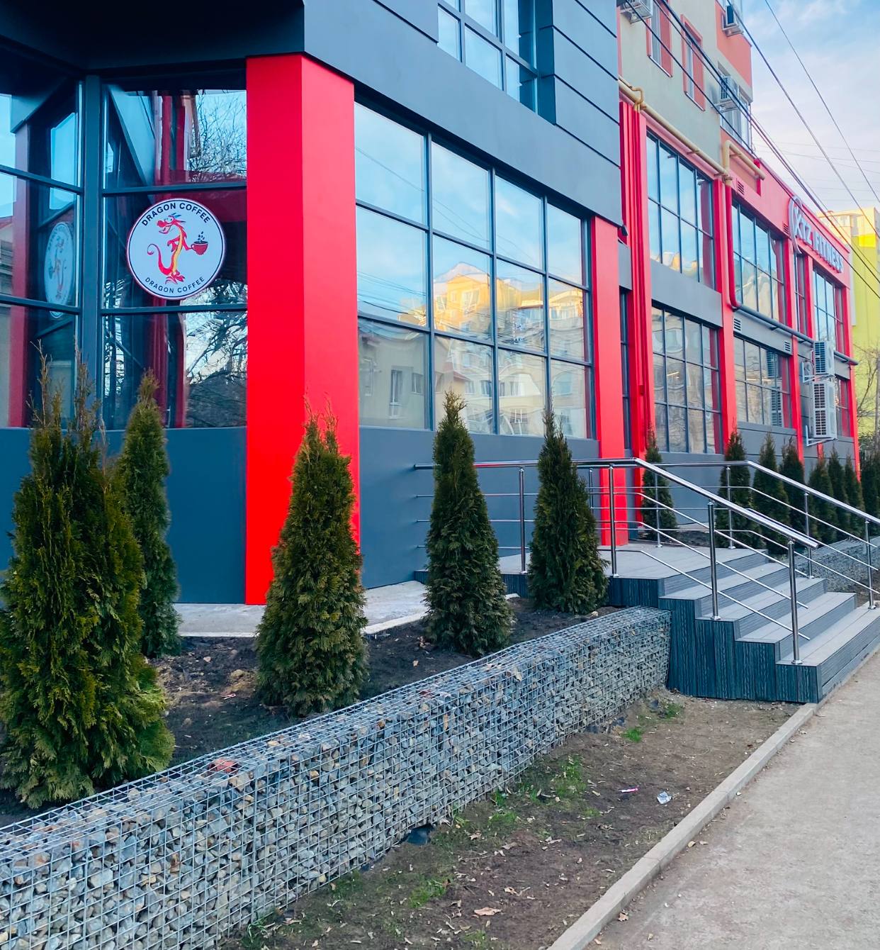 Modern storefront with bold red and blue facade, landscaped entrance with evergreen plantings