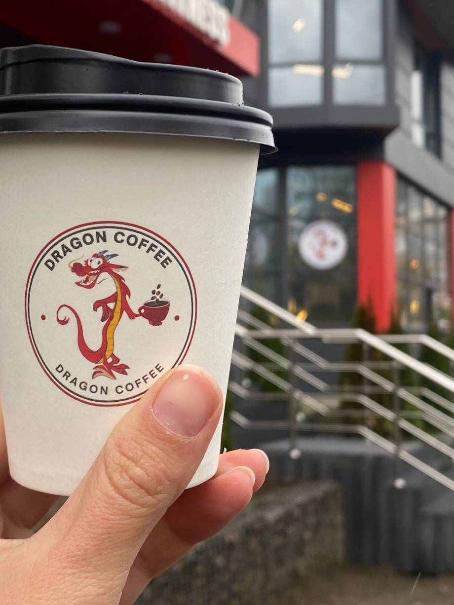 Dragon Coffee branded cup held in hand with storefront blurred in background
