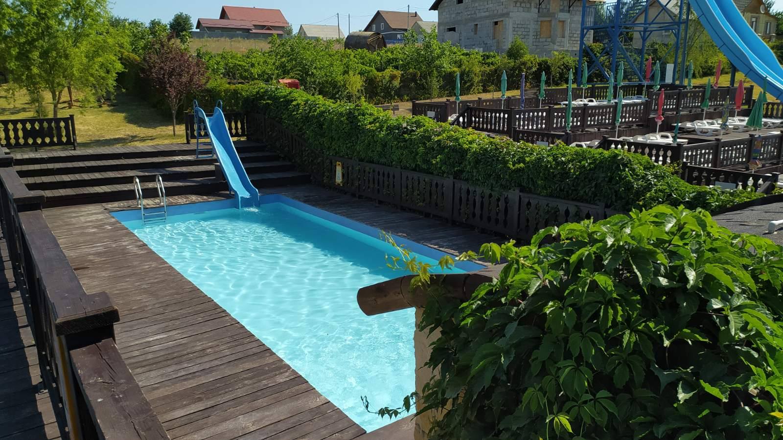 Outdoor pool with wooden deck and recreational area surrounded by green landscape