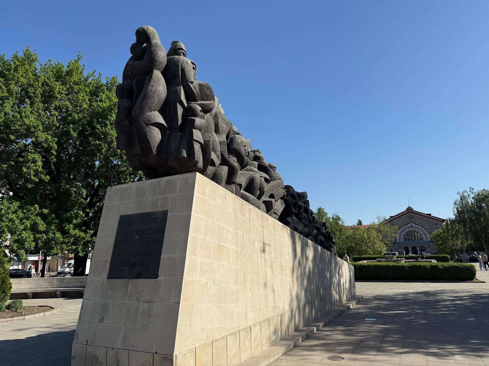 Public monument sculpture with bronze figures on stone base in park setting