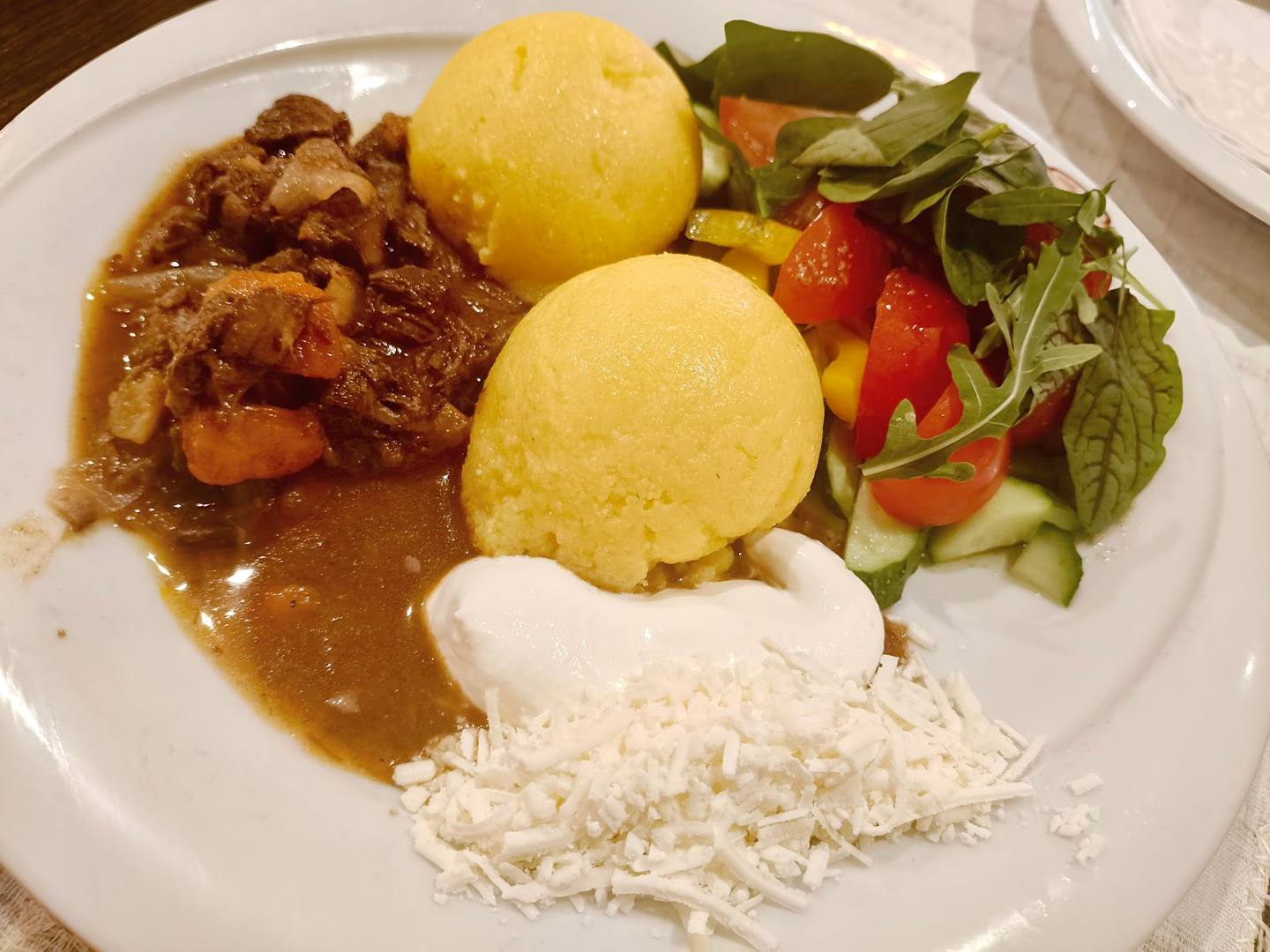 Braised meat with polenta, fresh salad and white cheese on white plate