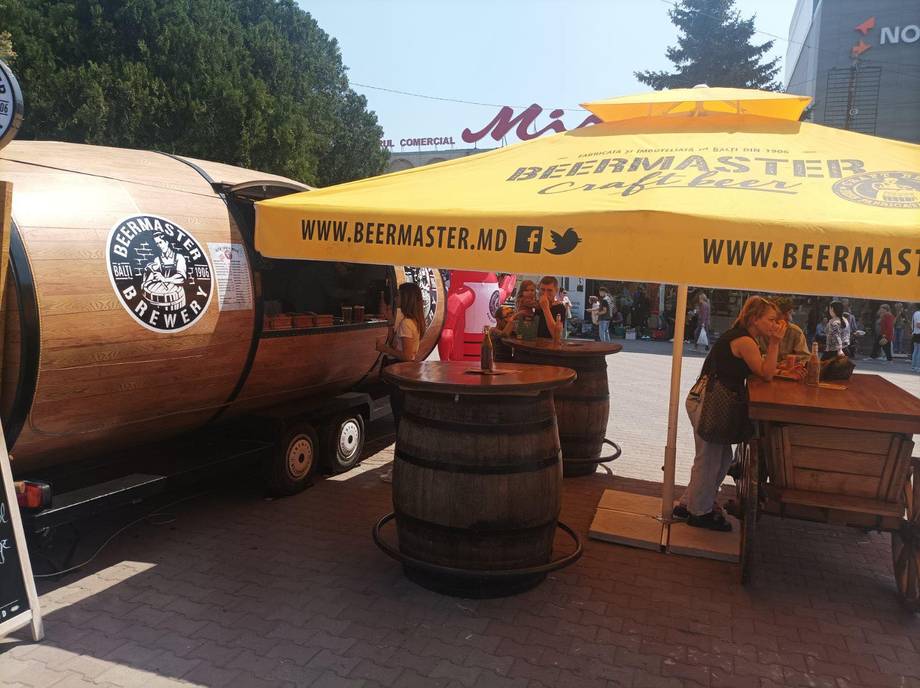 BeerMaster beer garden setup with wooden barrel tables and branded trailer