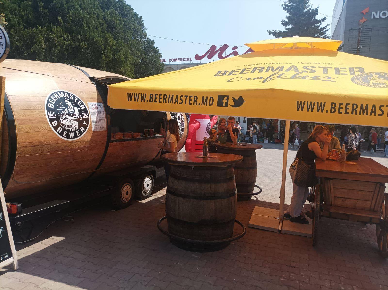 BeerMaster beer garden setup with wooden barrel tables and branded trailer