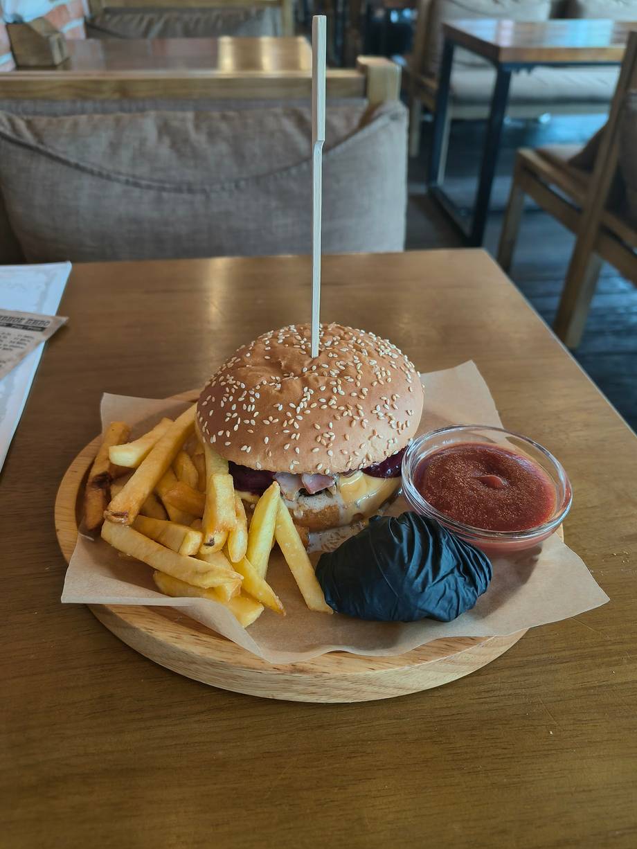Gourmet burger with sesame bun, fries, and dipping sauce on wooden board