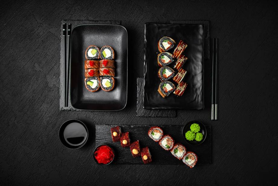Sushi and rolls arranged on black platters with chopsticks and condiments