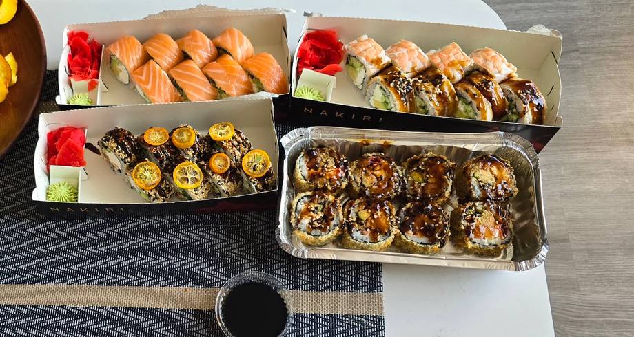 Assorted sushi and rolls plated in white takeout containers