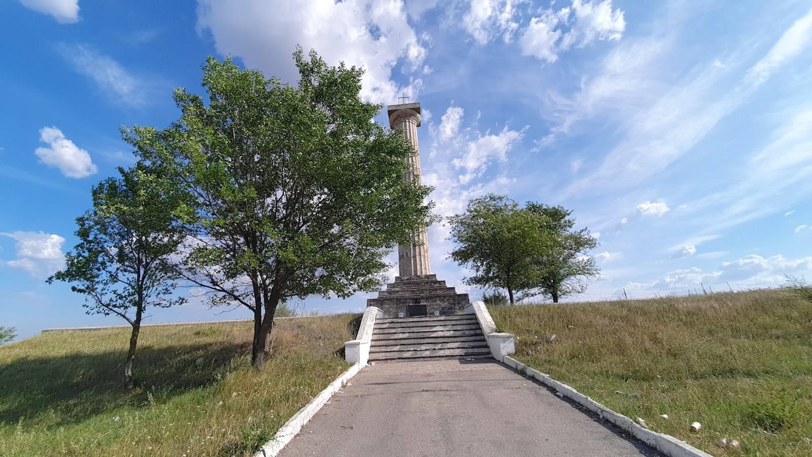 Monument on hillside with tree-lined approach road and open landscape