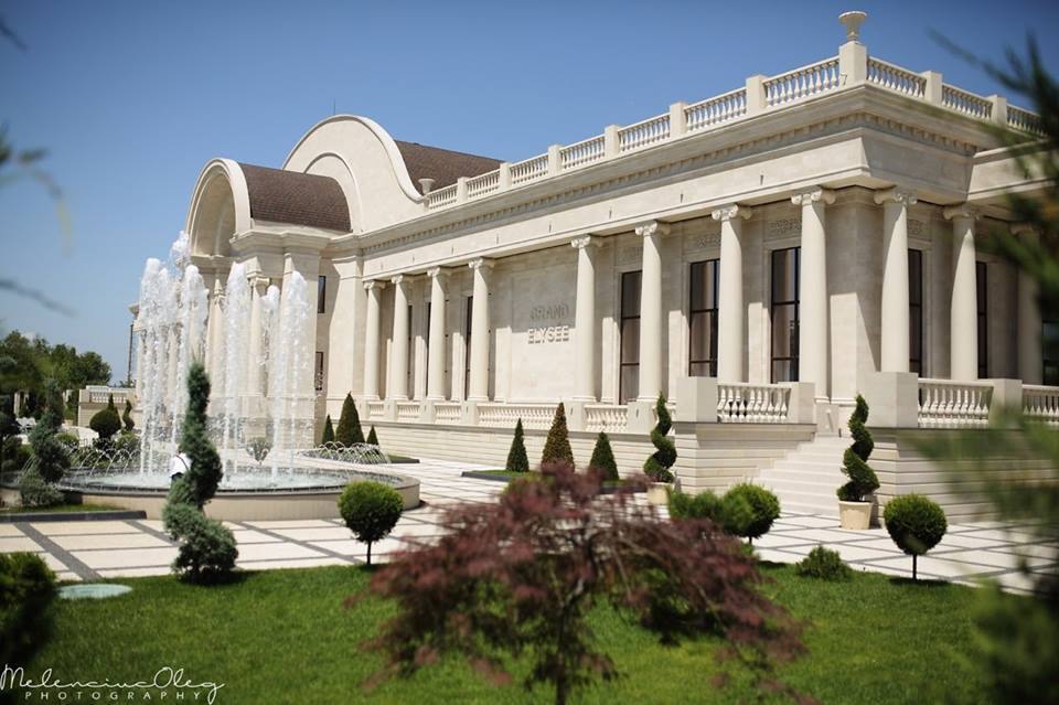 Classical mansion exterior with colonnade and manicured gardens under clear sky
