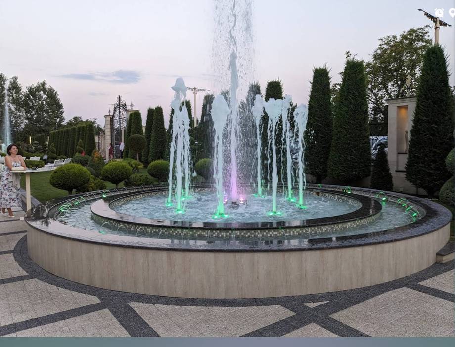 Illuminated fountain plaza with evergreen landscaping at dusk