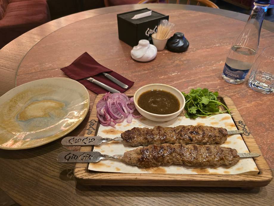 Grilled kebab platter with flatbread, herbs, and sauce on wooden table
