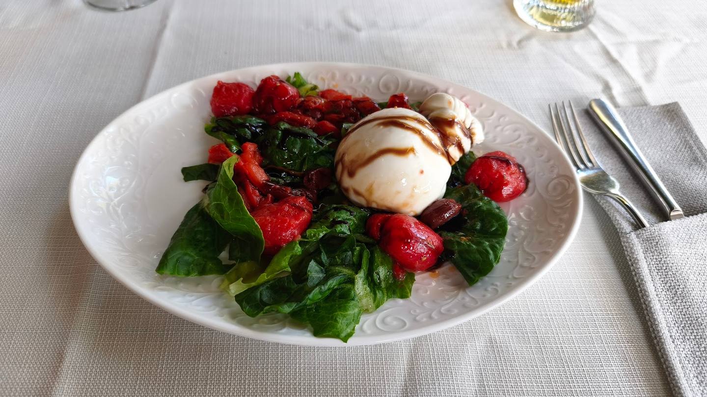 Gourmet salad with raspberries, burrata cheese and greens on white table setting