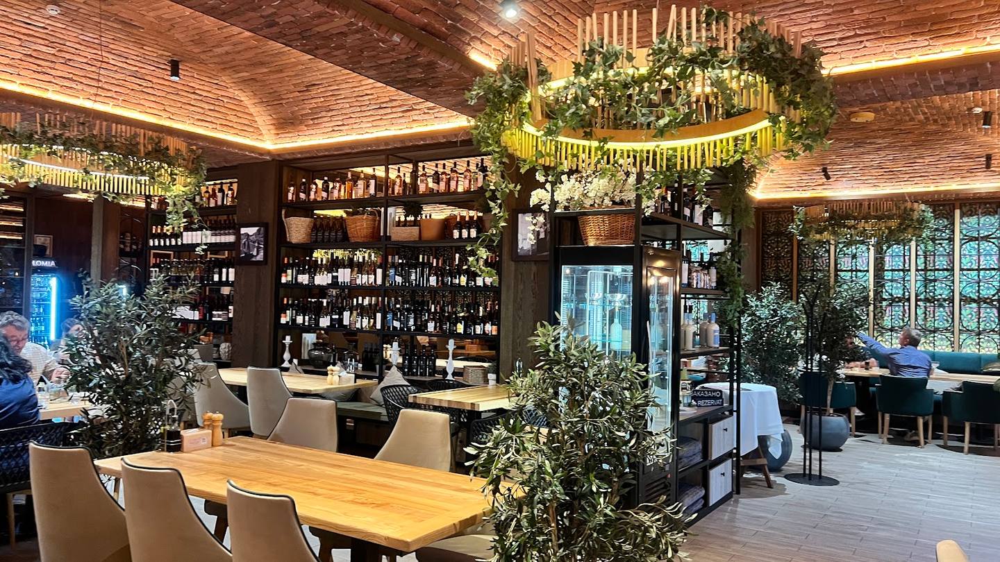 Modern wine bar interior with wooden tables, stocked bottles, and botanical decor