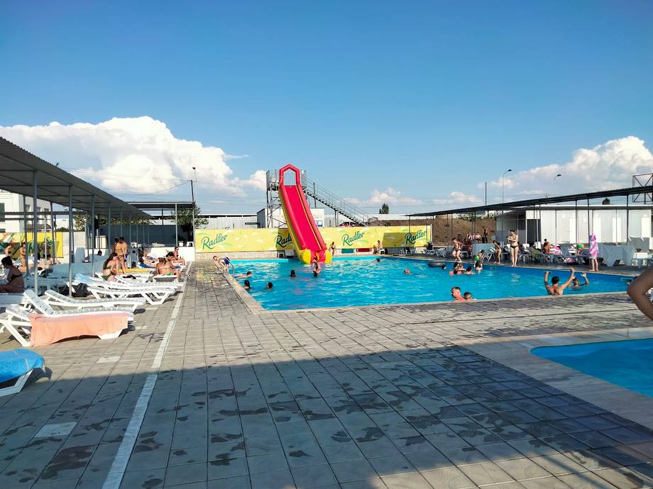 Outdoor water park with red slide, swimming pools, and recreational areas under clear sky
