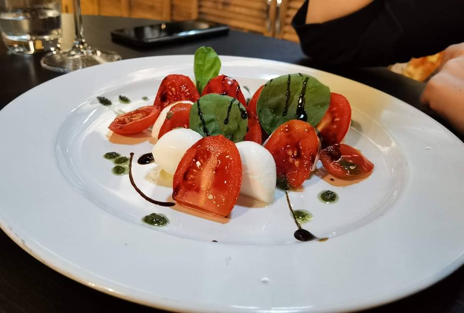 Caprese salad with tomato, mozzarella, and basil on white platter
