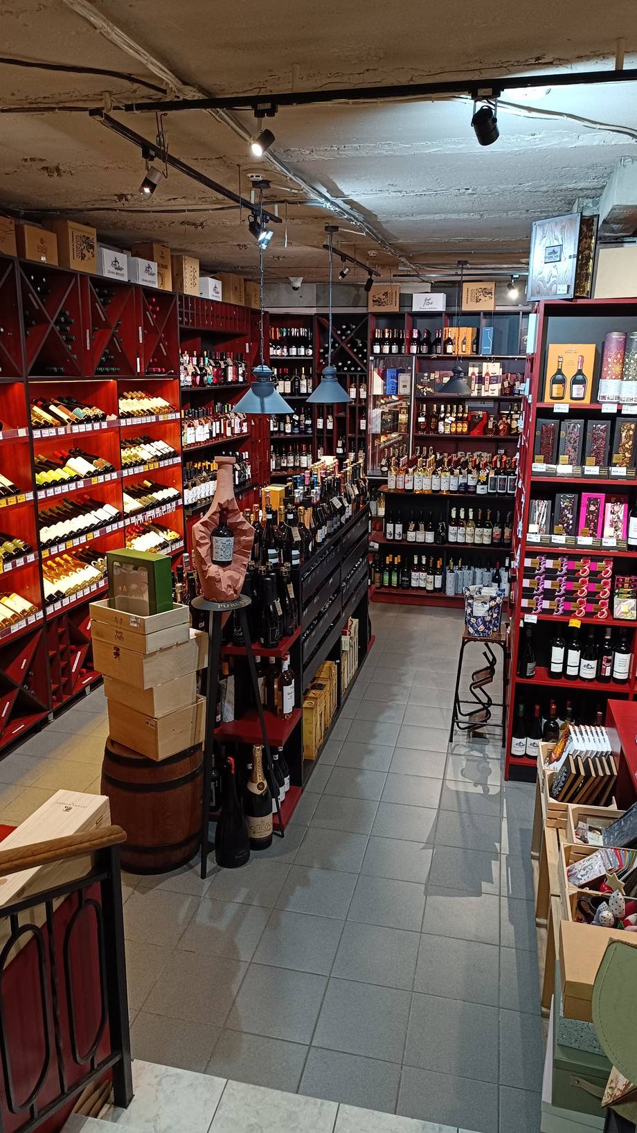 Wine shop interior with red shelving, bottles and product display along aisles