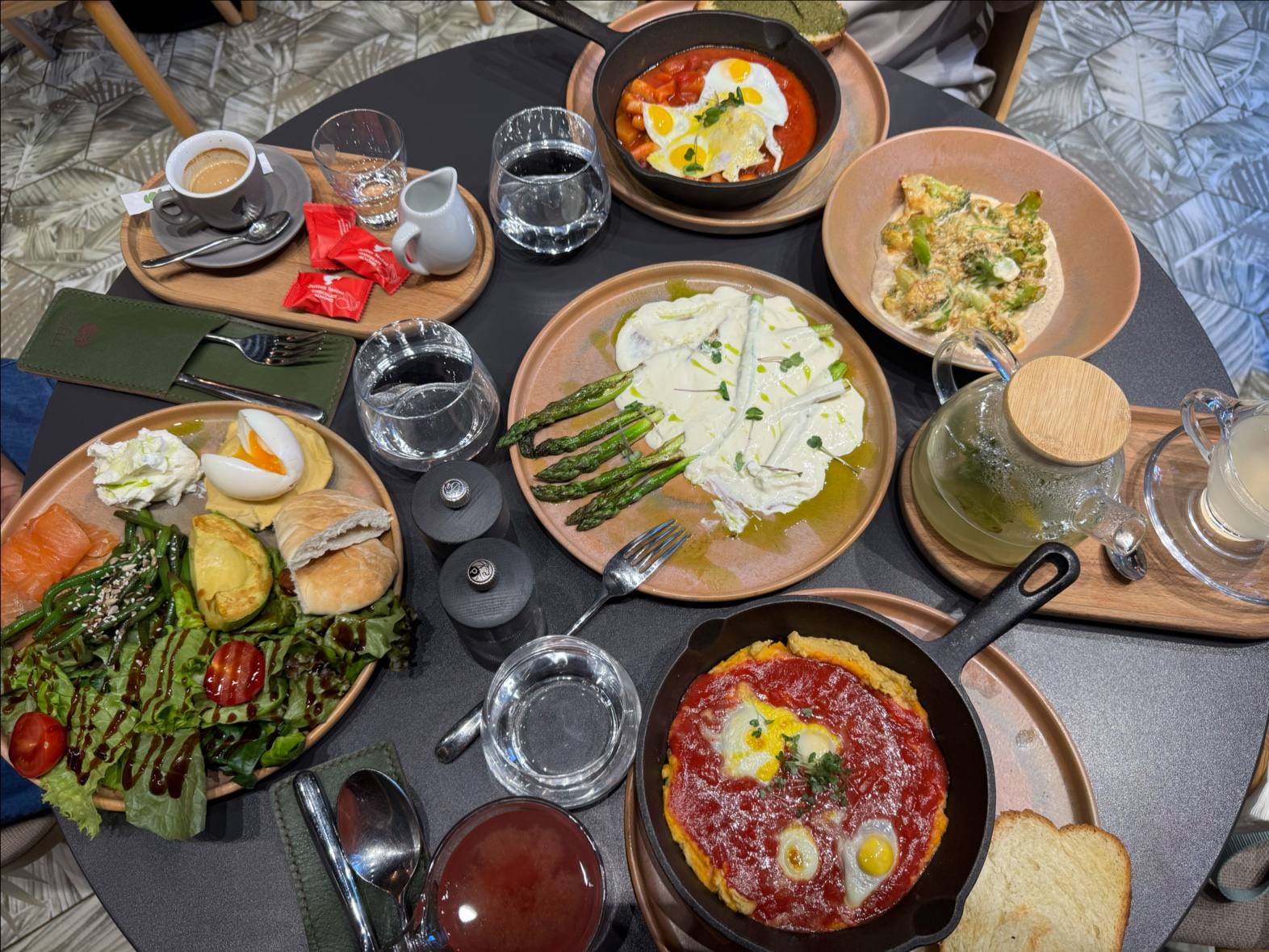 Overhead spread of shared dishes including salad, pasta, and baked egg with bread and wine
