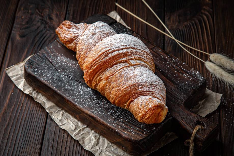 Fresh croissant dusted with powdered sugar on dark wooden board