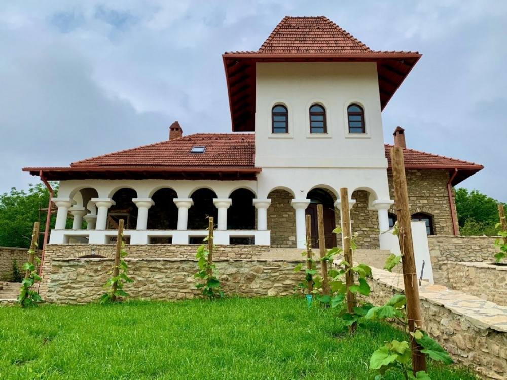 Historic stone monastery with tower, arched windows, and surrounding green grounds