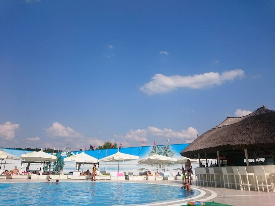 Aquatic water park with pool, slides, and thatched-roof pavilions under clear sky