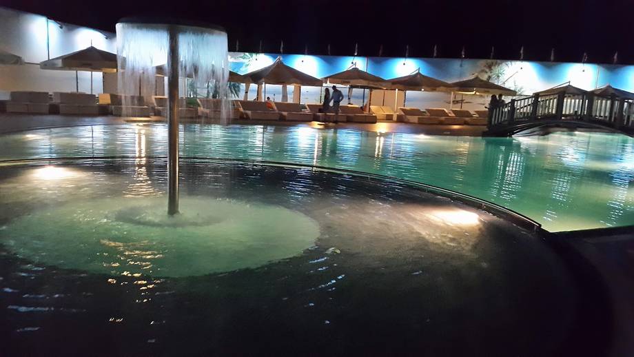 Illuminated thermal pool complex at night with wooden spa structures and turquoise water