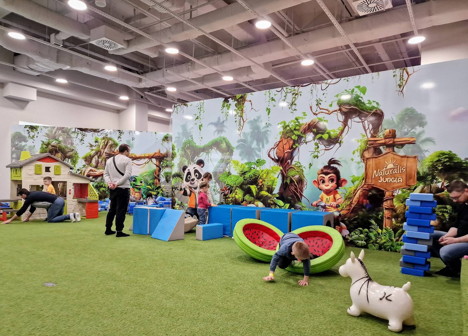 Indoor play area with jungle-themed decor, artificial grass, and activity stations for children