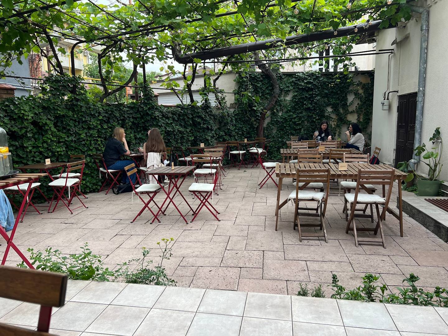Outdoor terrace with shade canopy, wooden tables and varied seating in a courtyard garden setting