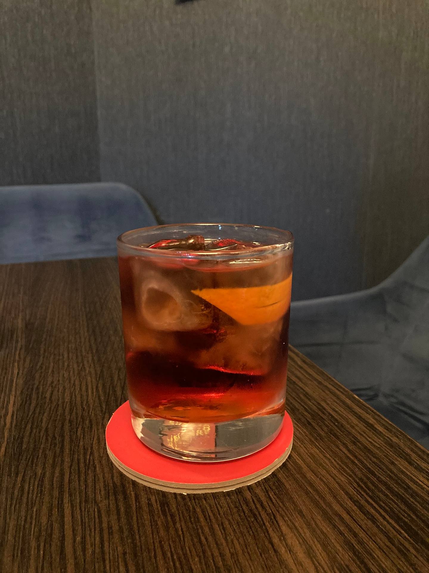 Craft cocktail with ice and coral coaster on wooden table