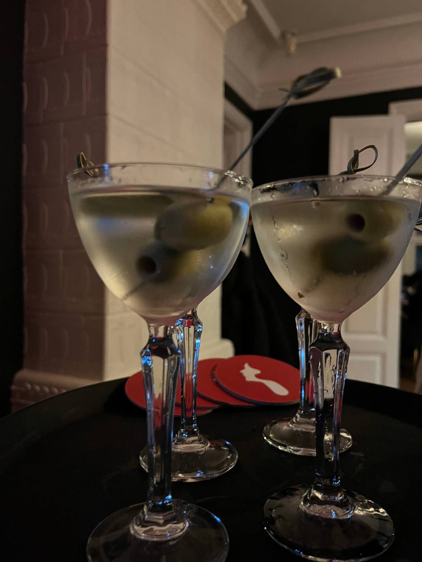 Two martinis with olive garnish on black table in bar setting