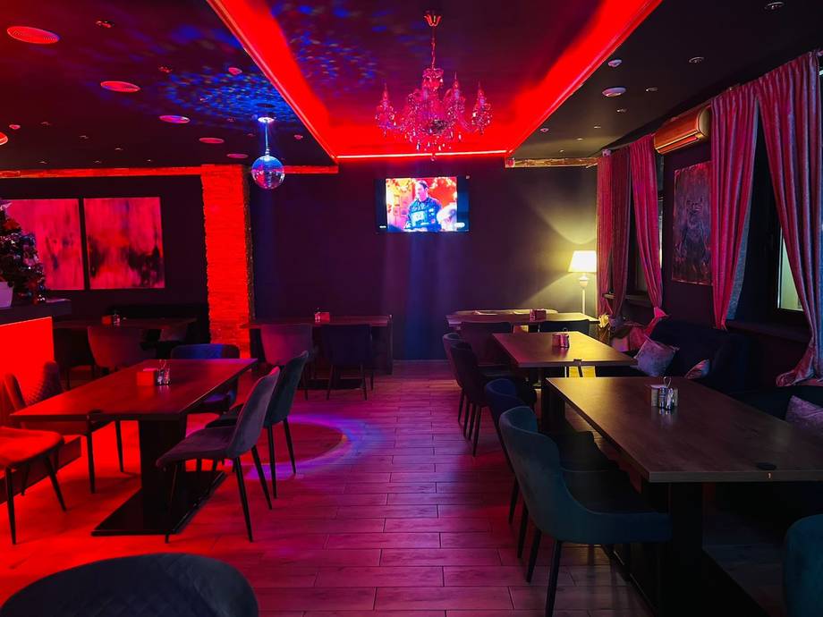 Nightclub interior with red neon lighting, bar seating, and atmospheric ambiance