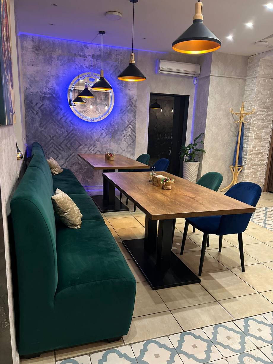 Modern dining lounge with green velvet seating, wood table, and blue neon accent lighting