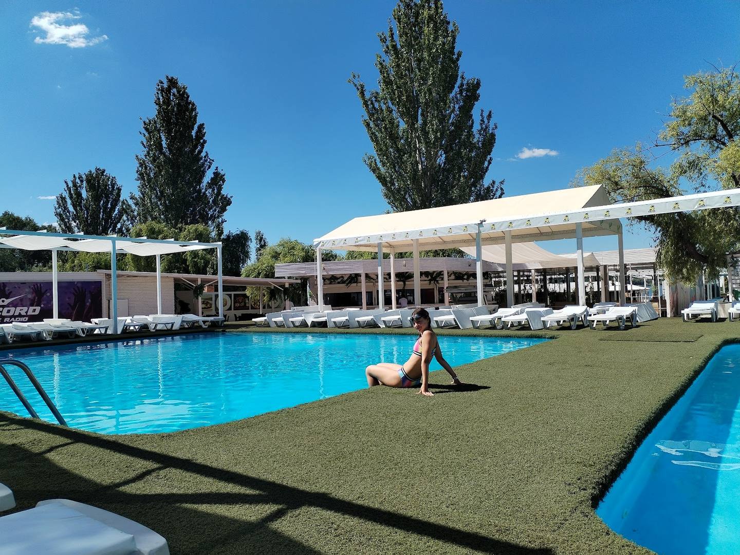 Open-air pool complex with lounge seating and tensile roof canopy under clear sky