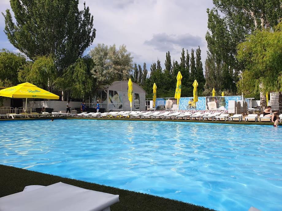 Open-air swimming pool with yellow umbrellas, yellow diving platforms, and poplar-lined grounds