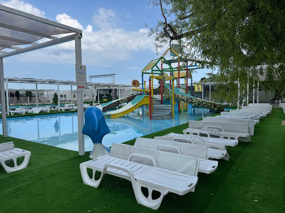 Family pool complex with water slide, loungers, and playground on manicured lawn