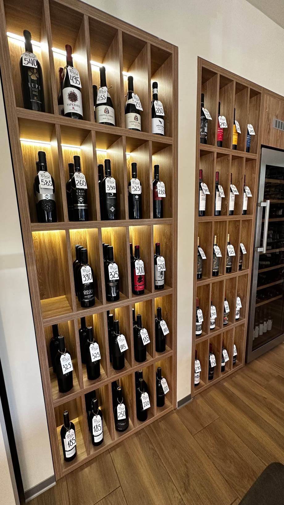 Modern wooden wine display wall with illuminated shelving showcasing curated wine bottles