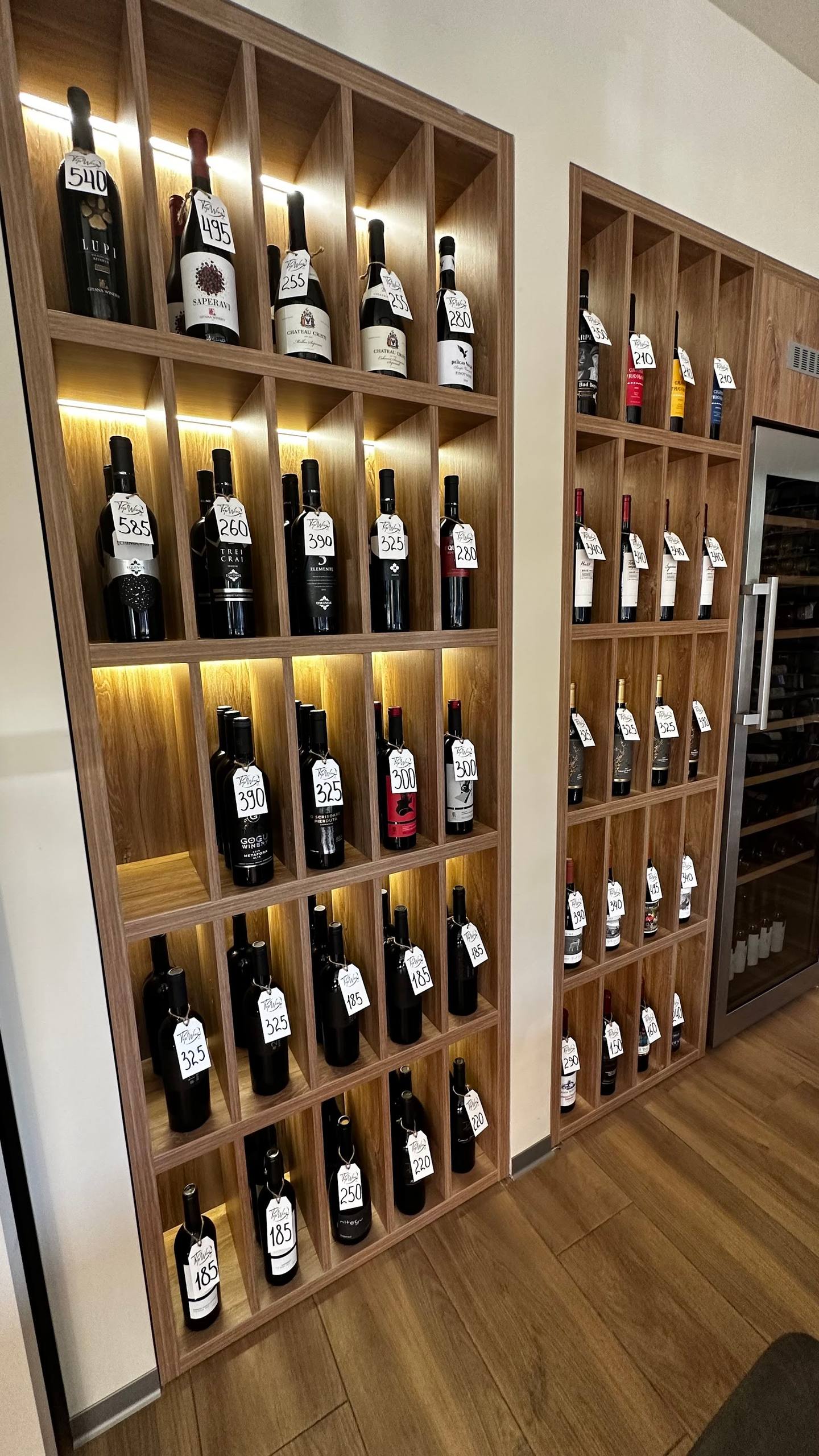 Modern wooden wine display wall with illuminated shelving showcasing curated wine bottles