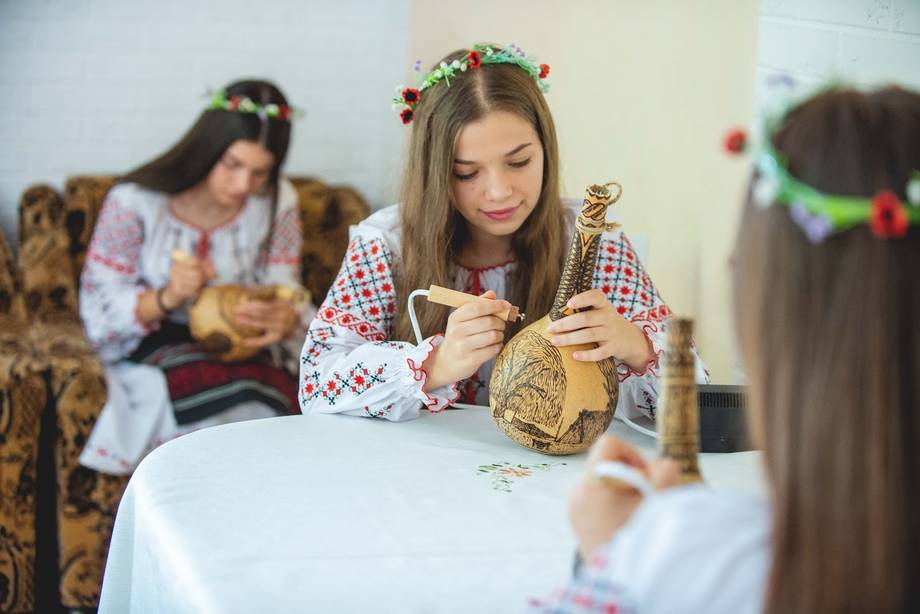 Children in traditional embroidered shirts crafting or participating in a cultural activity indoors